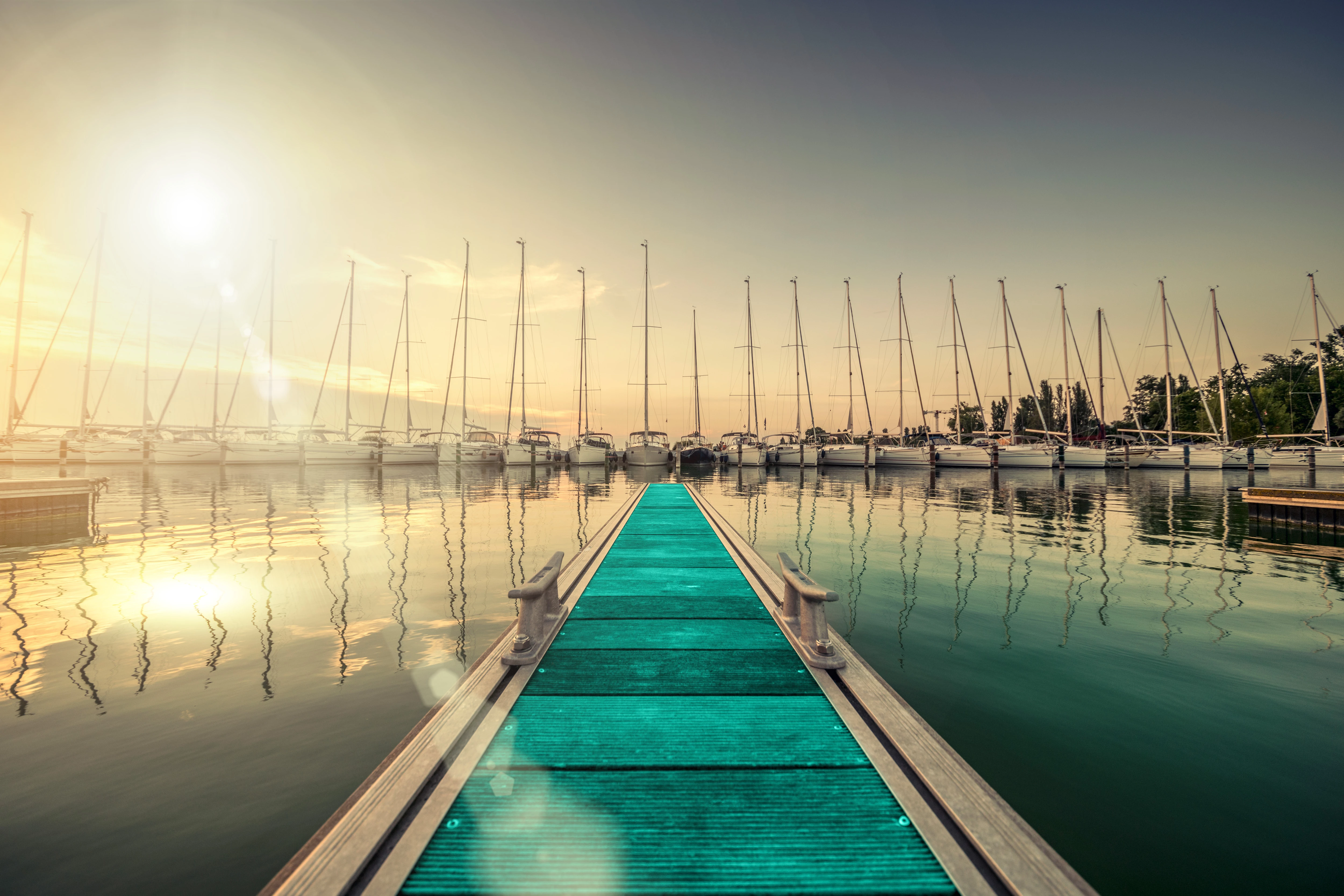 View along the pier of a harbor in golden sunlight with sailboats in the background. Sigh